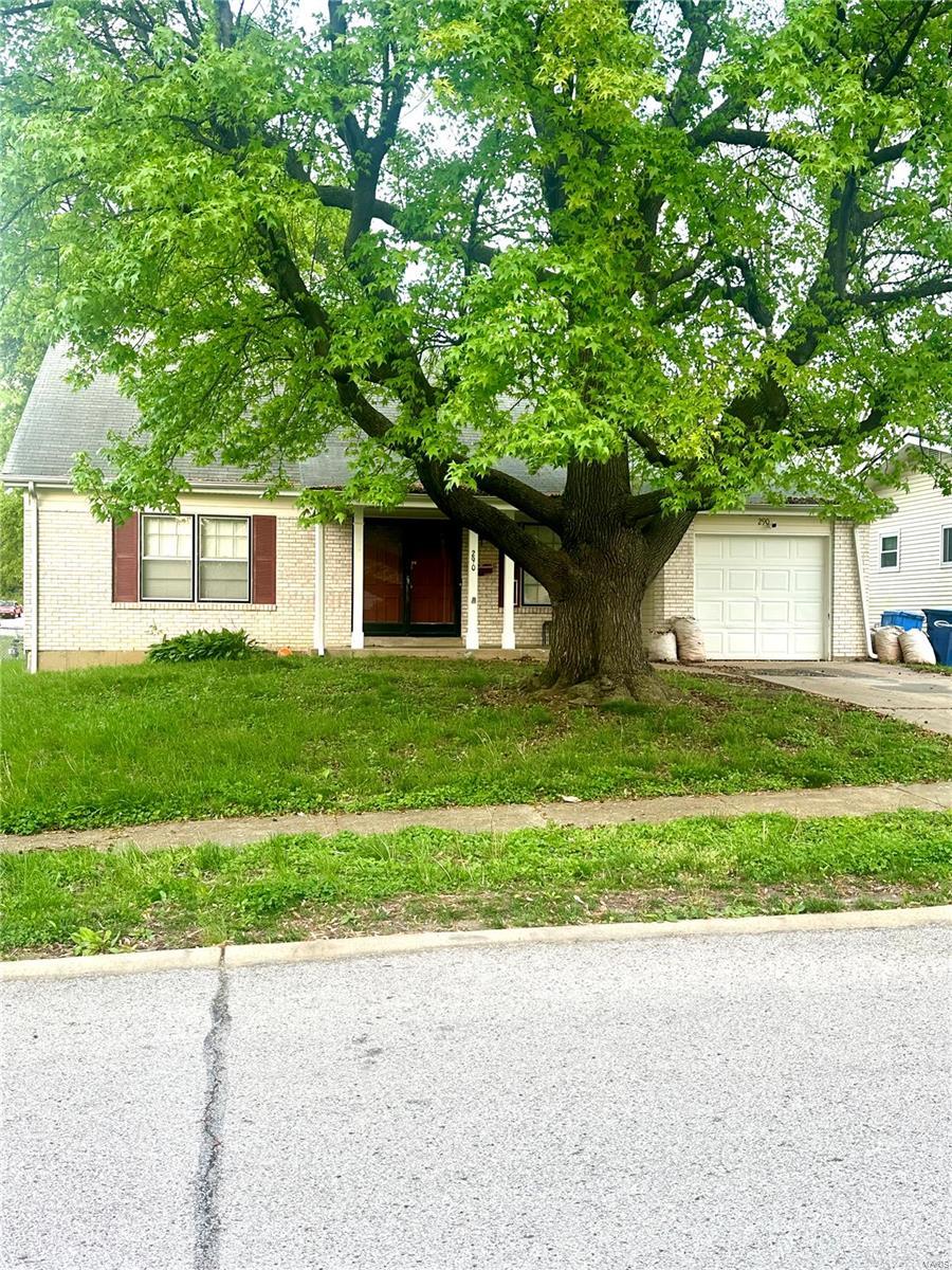 view of property hidden behind natural elements featuring concrete driveway, brick siding, an attached garage, and a front yard