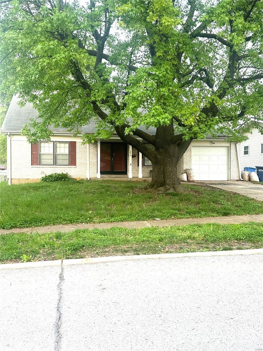 obstructed view of property with concrete driveway, brick siding, an attached garage, and a front lawn