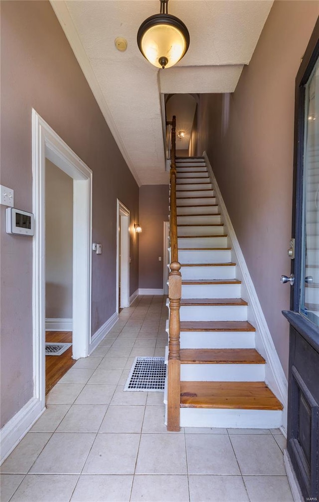 stairway with tile patterned flooring, ornamental molding, and baseboards