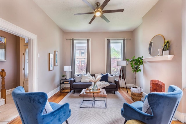 living room featuring baseboards, a ceiling fan, light wood-type flooring, and a textured ceiling