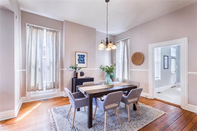 dining space featuring baseboards, visible vents, hardwood / wood-style floors, and a chandelier