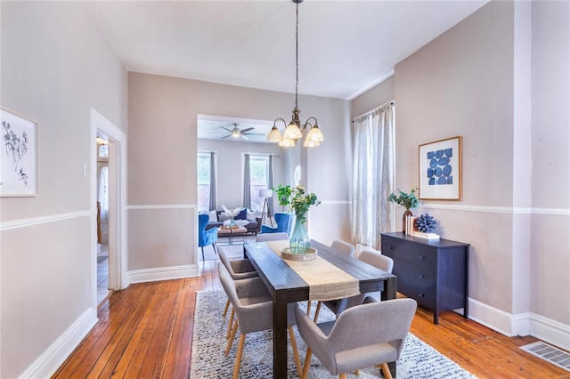 dining area with baseboards, ceiling fan with notable chandelier, hardwood / wood-style floors, and visible vents
