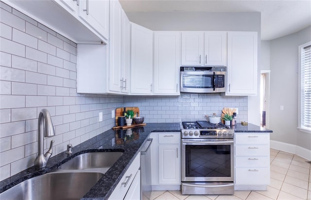 kitchen featuring appliances with stainless steel finishes, a sink, dark stone countertops, white cabinetry, and tasteful backsplash