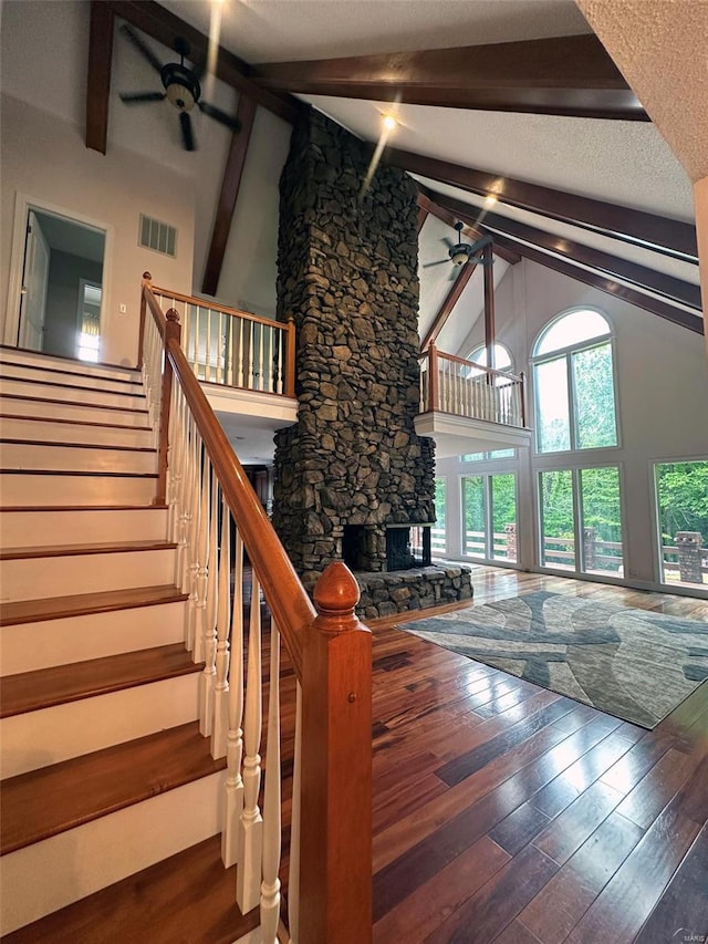 living room featuring ceiling fan, visible vents, a stone fireplace, and high vaulted ceiling