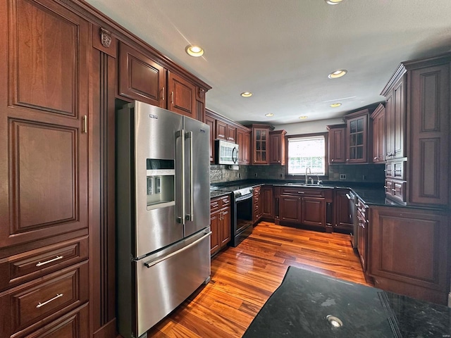 kitchen featuring tasteful backsplash, wood finished floors, a sink, glass insert cabinets, and stainless steel appliances