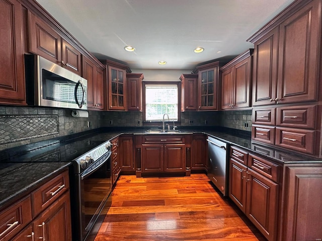 kitchen featuring glass insert cabinets, backsplash, appliances with stainless steel finishes, a sink, and light wood-style floors