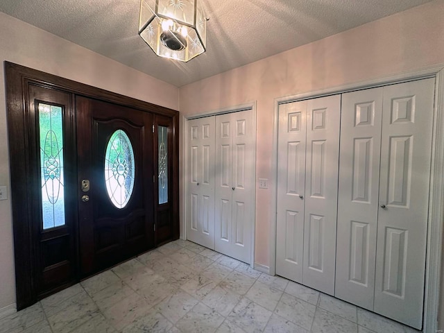 foyer entrance featuring a textured ceiling, baseboards, and marble finish floor