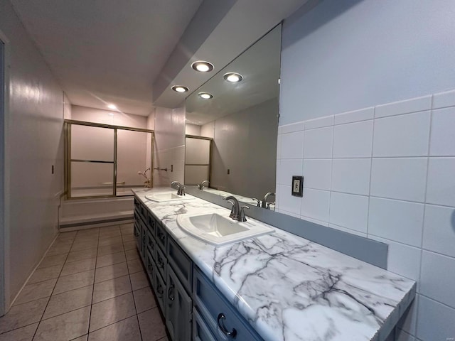full bath with double vanity, a sink, tile patterned flooring, and bath / shower combo with glass door