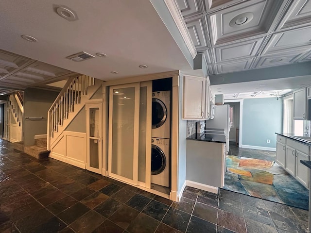 clothes washing area with laundry area, stacked washing maching and dryer, stone tile floors, baseboards, and visible vents