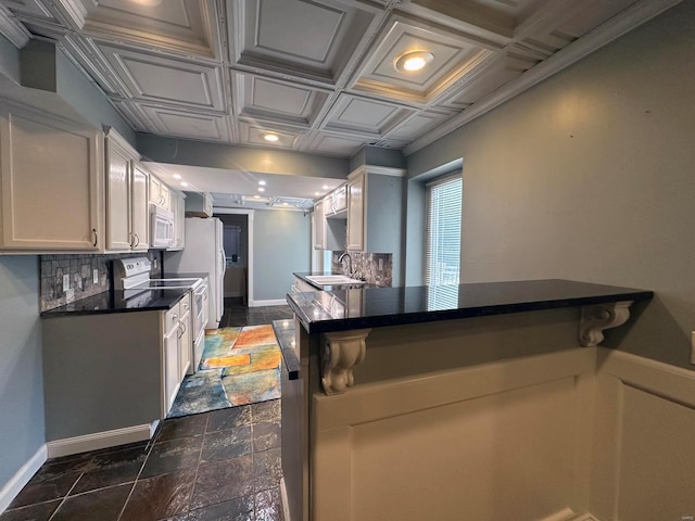kitchen featuring white appliances, baseboards, dark countertops, and a sink