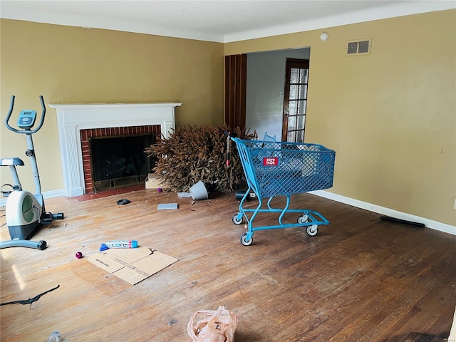 living room with baseboards, a brick fireplace, wood finished floors, and visible vents