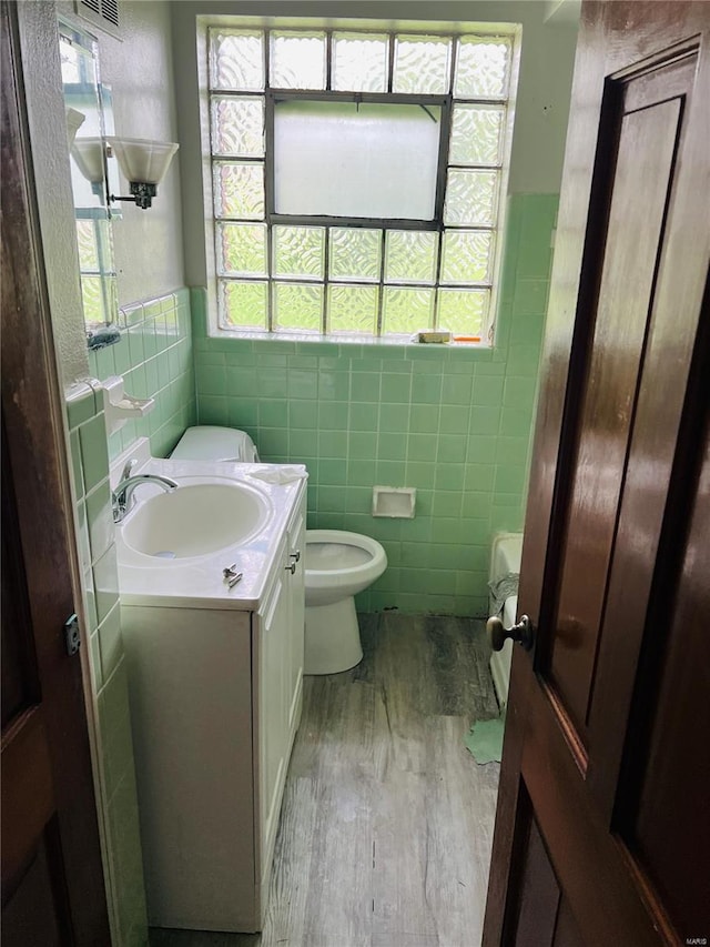 bathroom featuring vanity, visible vents, wood finished floors, toilet, and tile walls