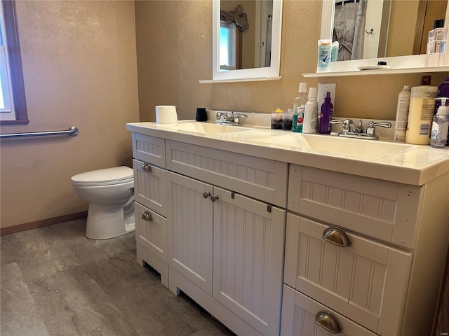full bathroom with double vanity, a sink, baseboards, toilet, and a textured wall