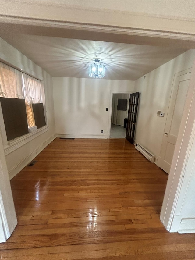 unfurnished room with baseboards, a baseboard radiator, hardwood / wood-style floors, and visible vents