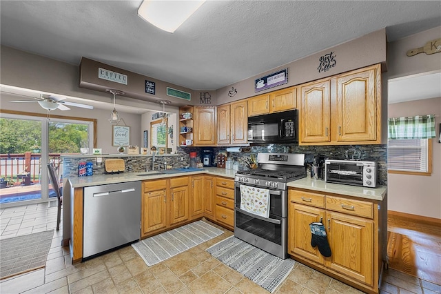 kitchen featuring a peninsula, a toaster, a sink, appliances with stainless steel finishes, and backsplash
