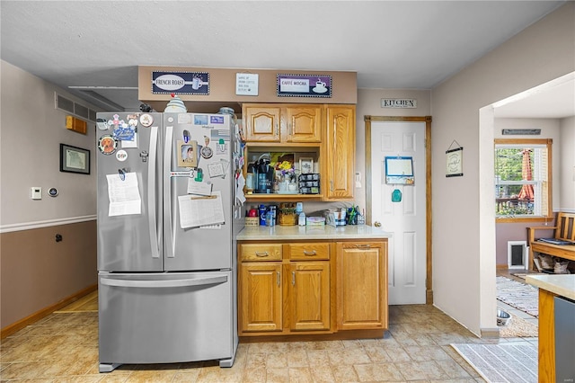 kitchen with light countertops, baseboards, freestanding refrigerator, and brown cabinets