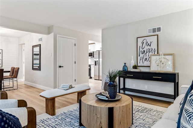 living area featuring baseboards, light wood-type flooring, and visible vents