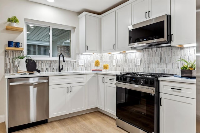 kitchen featuring appliances with stainless steel finishes, light countertops, light wood-style flooring, white cabinetry, and backsplash