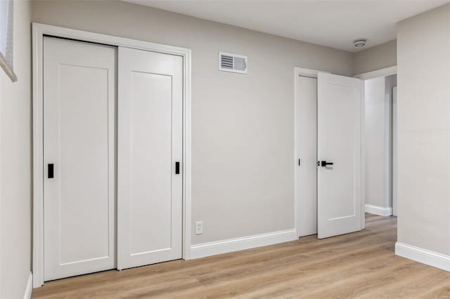 unfurnished bedroom with two closets, baseboards, visible vents, and light wood-style floors