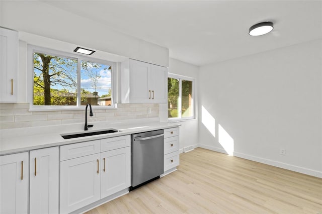kitchen featuring tasteful backsplash, dishwasher, a sink, baseboards, and light wood finished floors