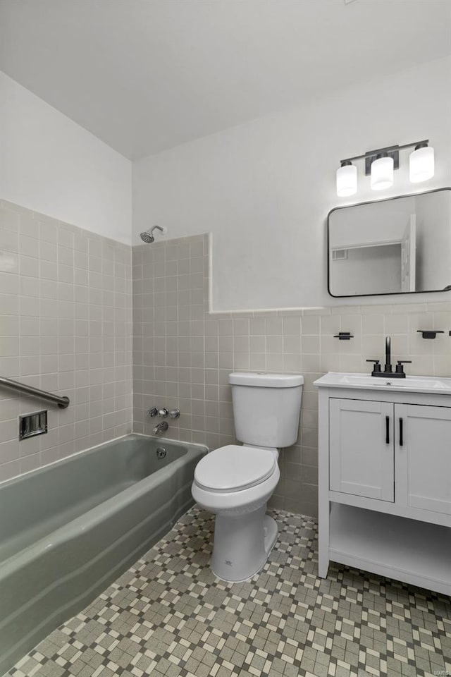 full bath featuring vanity, tub / shower combination, toilet, tile walls, and a wainscoted wall