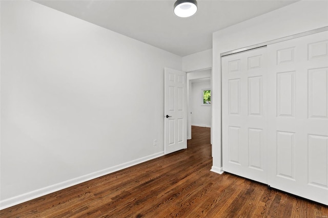 unfurnished bedroom featuring dark wood-type flooring, baseboards, and a closet