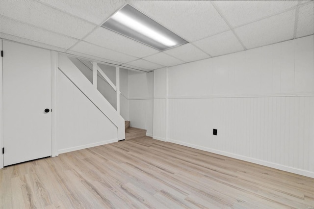 finished below grade area with stairway, baseboards, a drop ceiling, and wood finished floors