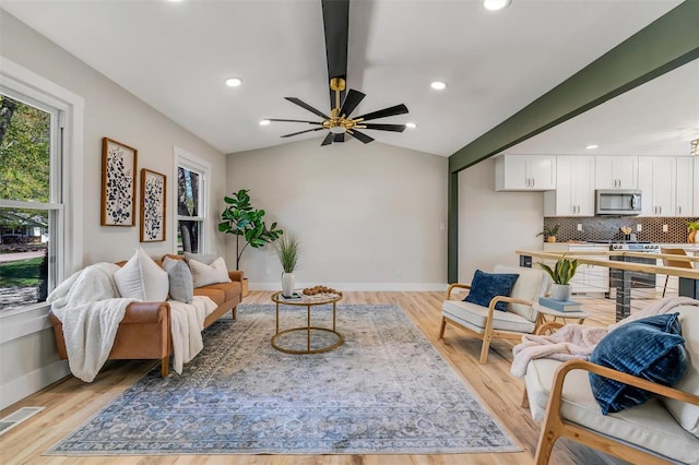 living area with visible vents, baseboards, vaulted ceiling with beams, a ceiling fan, and light wood-style flooring