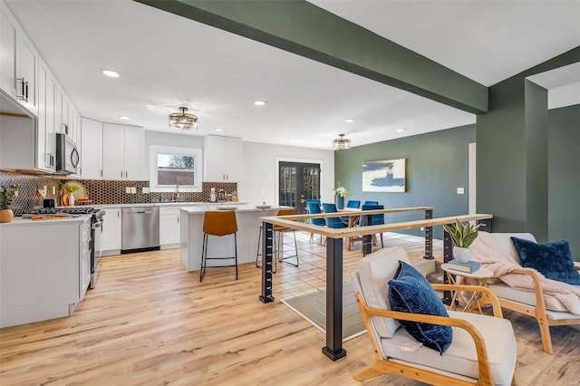 kitchen with decorative backsplash, light countertops, white cabinets, light wood finished floors, and appliances with stainless steel finishes