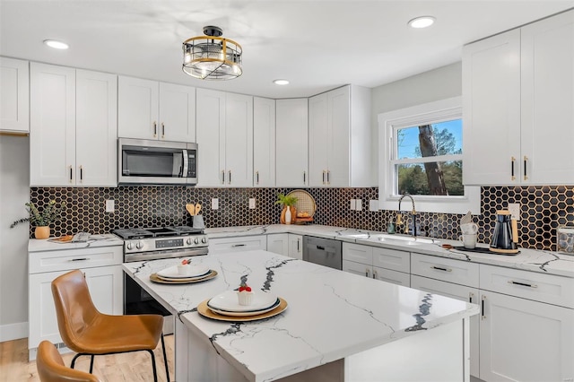 kitchen with a sink, white cabinetry, light stone countertops, and stainless steel appliances