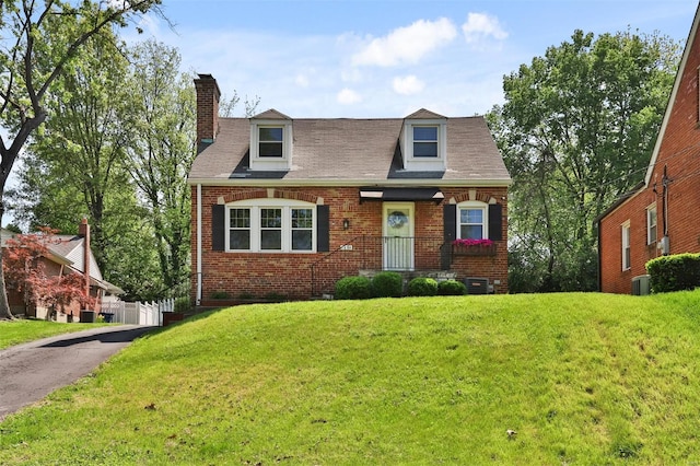 cape cod home featuring brick siding, a shingled roof, a front lawn, and a chimney