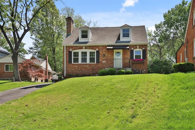 cape cod home with brick siding, a chimney, and a front lawn