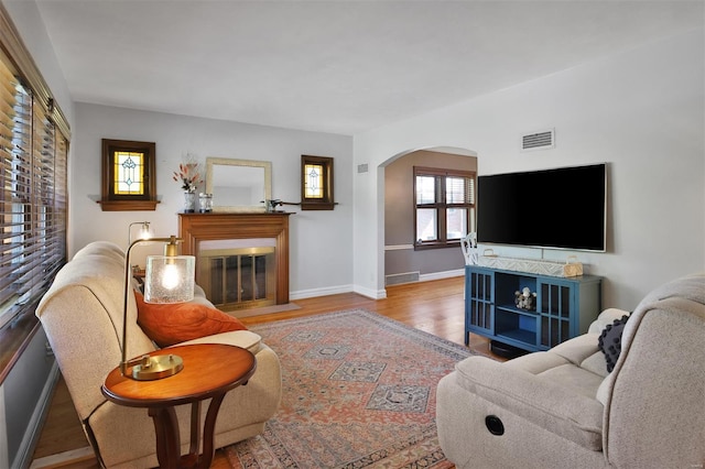 living area featuring arched walkways, baseboards, a fireplace with flush hearth, wood finished floors, and visible vents
