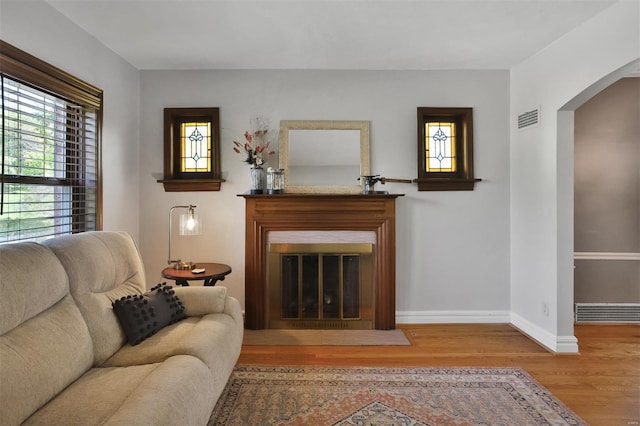 living room with arched walkways, baseboards, a fireplace with flush hearth, wood finished floors, and visible vents