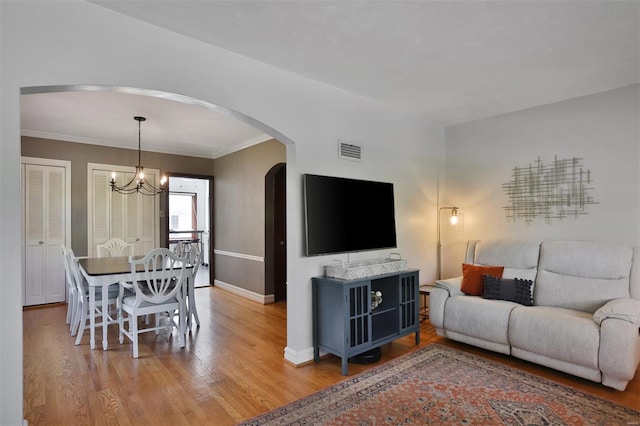 living area with visible vents, baseboards, a chandelier, arched walkways, and light wood finished floors