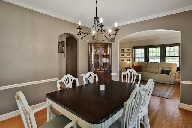 dining space with arched walkways, wood finished floors, baseboards, a notable chandelier, and ornamental molding