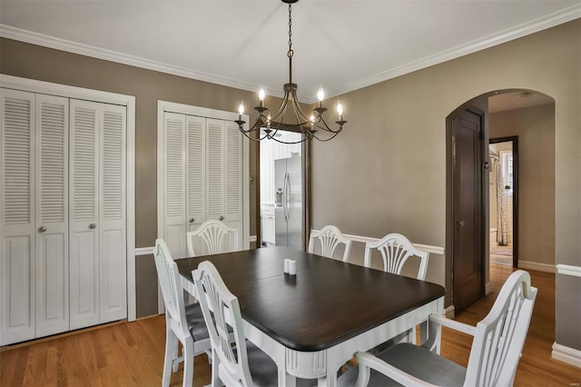 dining space featuring crown molding, arched walkways, a chandelier, and light wood-type flooring