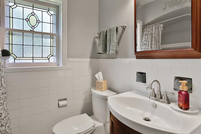 bathroom featuring vanity, toilet, a shower with shower curtain, a wainscoted wall, and tile walls
