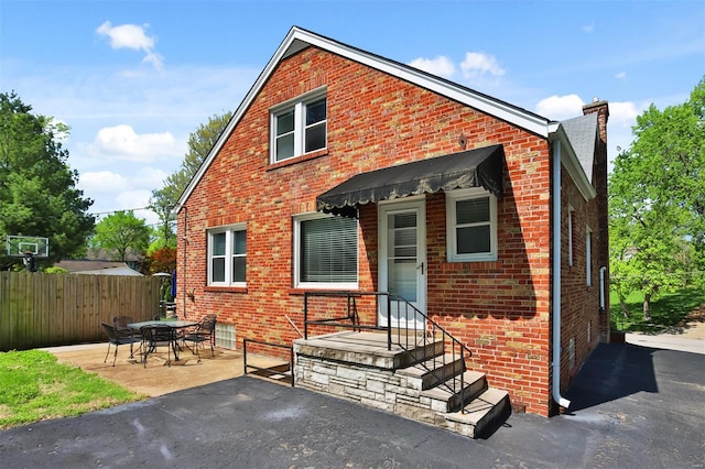 back of property with brick siding, fence, a chimney, and a patio area