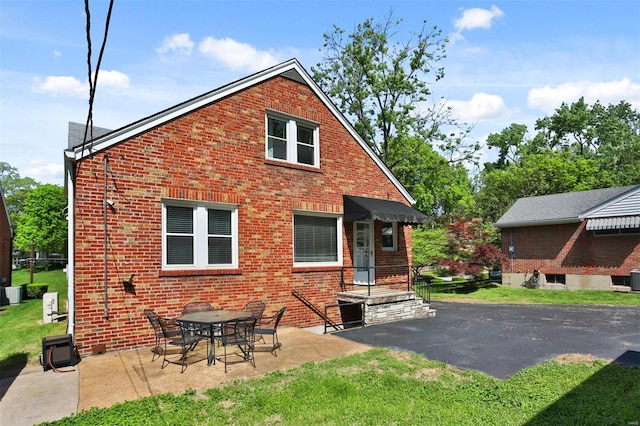 back of house featuring brick siding, central AC, a yard, and a patio
