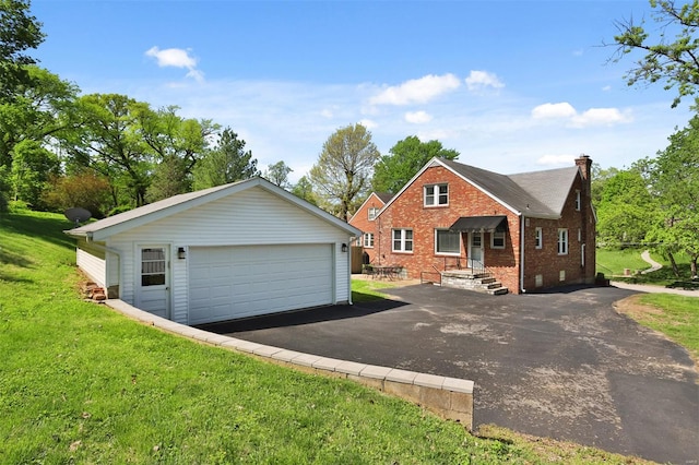 view of front of house with an outdoor structure, a front yard, a chimney, brick siding, and a detached garage