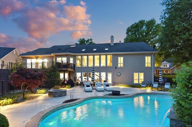 back of property at dusk featuring a fenced in pool, a chimney, a patio area, a balcony, and a fire pit