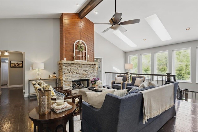 living room with ceiling fan, high vaulted ceiling, a stone fireplace, a skylight, and hardwood / wood-style flooring