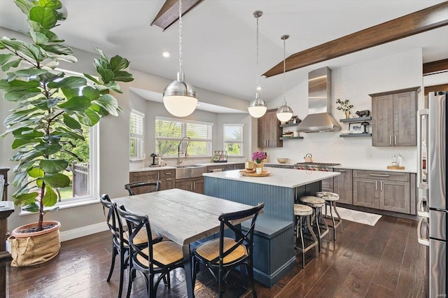 kitchen featuring wall chimney range hood, a kitchen island, dark wood finished floors, light countertops, and vaulted ceiling with beams