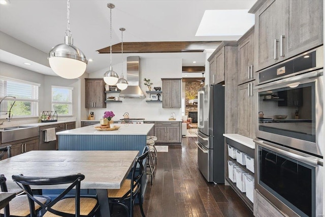 kitchen featuring a kitchen island, dark wood-style floors, wall chimney range hood, light countertops, and stainless steel appliances