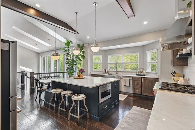 kitchen with a kitchen bar, a sink, lofted ceiling, stainless steel appliances, and wall chimney exhaust hood