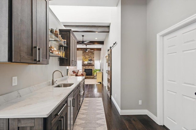 kitchen featuring dark wood-style flooring, dark brown cabinetry, a sink, a fireplace, and a ceiling fan