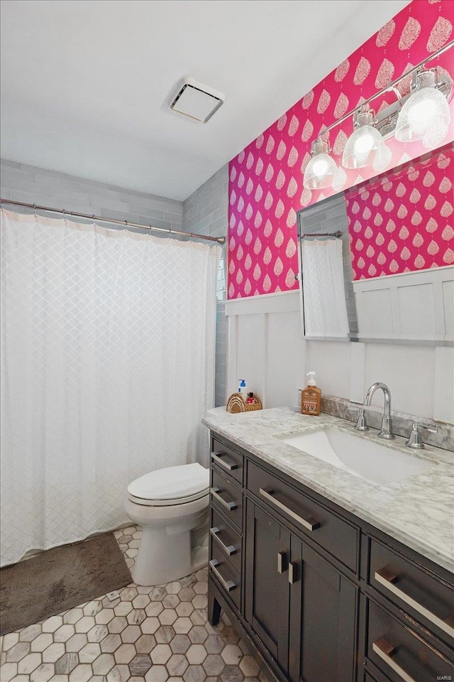 bathroom featuring visible vents, wainscoting, vanity, toilet, and wallpapered walls