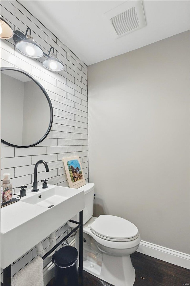 half bathroom with backsplash, visible vents, wood finished floors, baseboards, and toilet