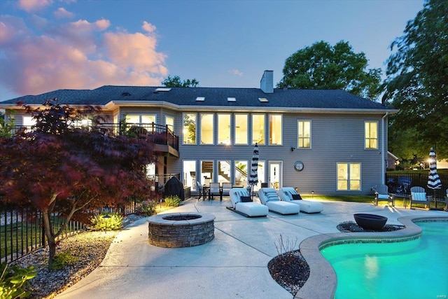 back of property featuring a chimney, a patio area, fence, a fenced in pool, and an outdoor fire pit